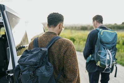 Rear view of male friends with backpacks walking by van