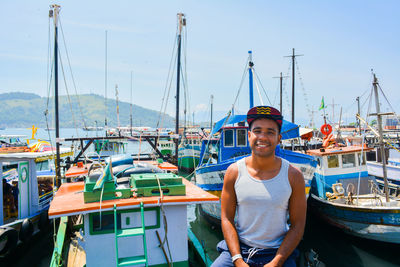 Portrait of young man sitting against boats moored at harbor