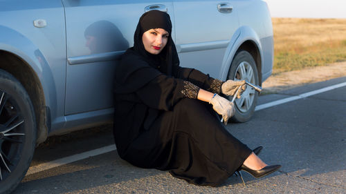 Full length of woman in burka sitting by car on road