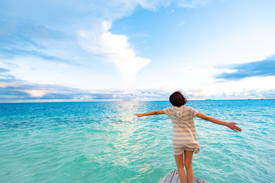 Rear view of woman with arms outstretched standing in boat on sea against sky