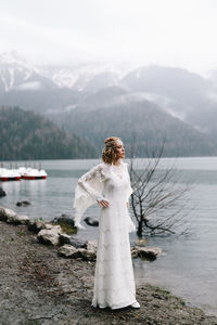 A beautiful young woman bride in a wedding lace dress stands in the middle of a lake and mountains