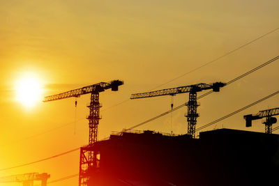 Silhouette cranes at construction site against sky during sunset