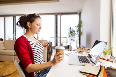 Smiling woman with coffee to go at home office