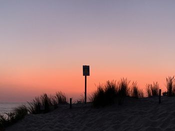 Silhouette wooden post on beach against clear sky during sunset