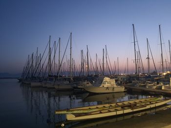 Sailboats moored in harbor at sunset