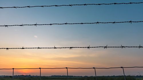 Silhouette of barbed wires against sky during sunset