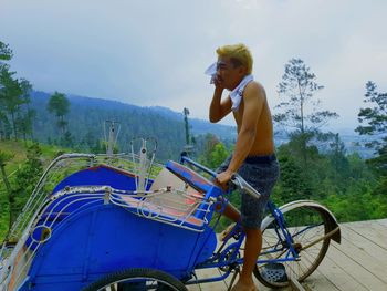 Side view of young man riding bicycle against sky