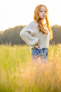 Beautiful young woman in a cozy knitted sweater outdoor in meadow in warm light sunset