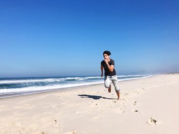 Full length of young man on beach against clear blue sky