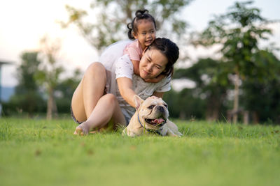 Woman piggybacking girl with dog on grass