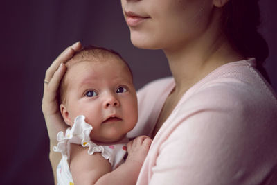 Mother in a white robe holds a small newborn daughter against the wall in the bedroom