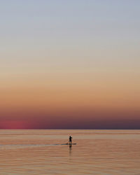 Silhouette person on sea against sky during sunset