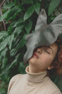 A beautiful plus size girl with red hair among the lush green branches of tropical plants. 