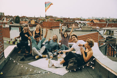 Happy male and female friends cheering on terrace while enjoying rooftop party in city