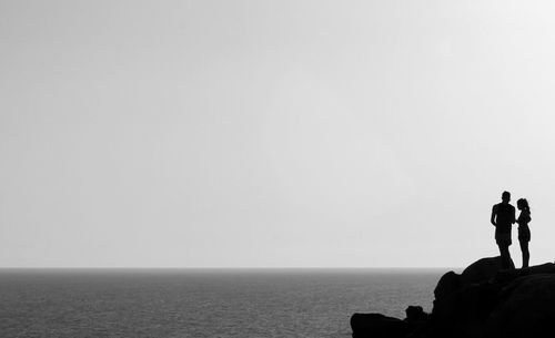 Rear view of silhouette friends standing by sea against clear sky