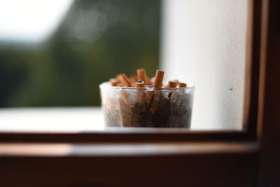 Close-up of cigarette butts in glass at window