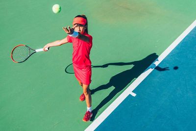 High angle view of girl practicing tennis while standing in court during sunny day