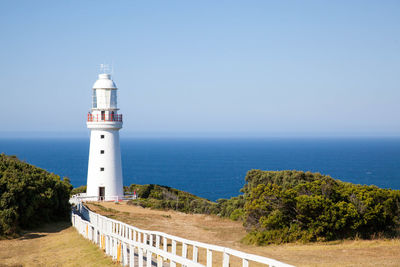 White lighthouse by sea against clear sky