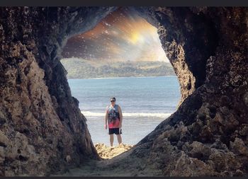 Rear view of woman standing on rock by sea against sky