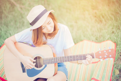 Young woman playing guitar on grassy field at park