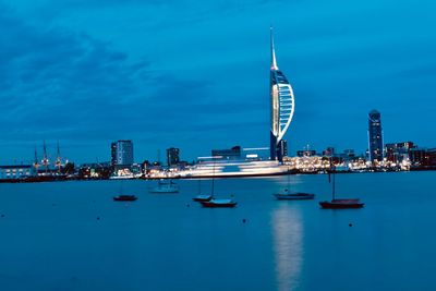 Sailboats in sea by modern buildings against blue sky