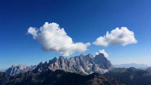 Low angle view of rocky mountains against cloudy blue sky on sunny day