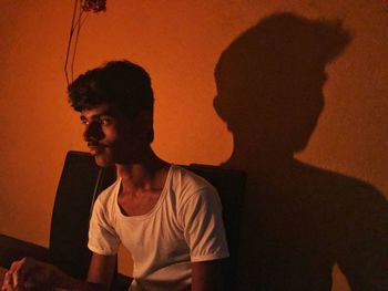 Portrait of young man looking away while sitting on wall