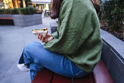 Woman holding sandwich sitting on bench