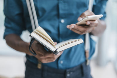 Young man using smart phone, holding note book