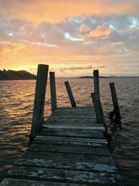 Wooden jetty in sea against sky during sunset