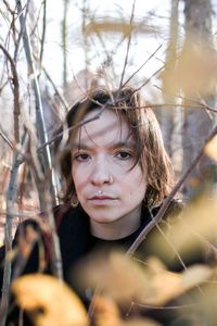 A young woman with a contemplative gaze stands among a vibrant array of fall foliage. 