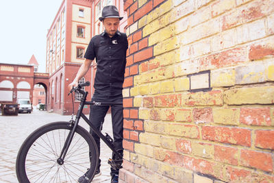 Man with bicycle standing on brick wall