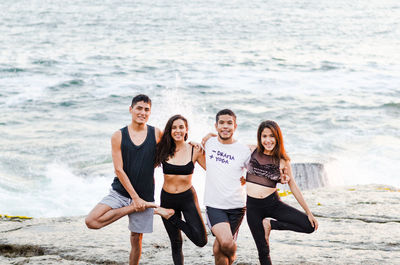 Portrait of smiling friends doing yoga at beach