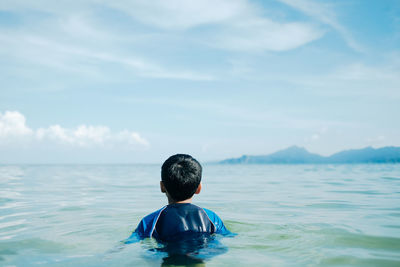 Rear view of boy in sea against sky