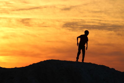 Silhouette boy standing on hill against cloudy sky during sunset