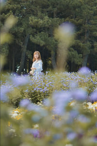 Woman standing amidst flowering plants and trees on field