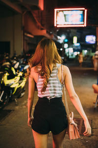 Rear view of woman walking on street in city at night