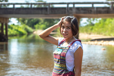 Portrait of smiling woman standing in river against bridge