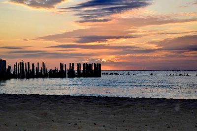 Wooden posts on beach against sky during sunset