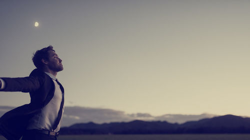 Side view of young man standing against sky during sunset