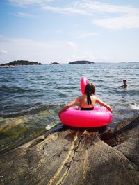 Rear view of woman on rock by sea against sky