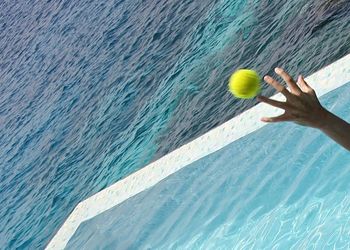 Cropped image of hand throwing ball in swimming pool