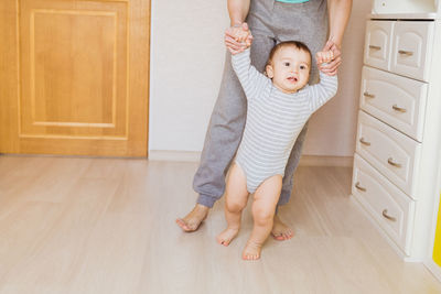 Low section of mother with baby standing on floor at home