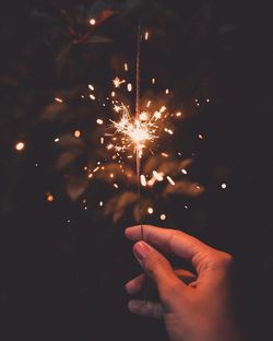 Cropped image of woman holding illuminated sparkler at night