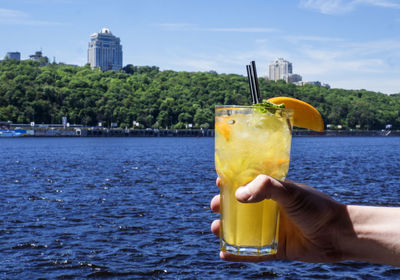 Close-up of hand holding drink by sea against sky