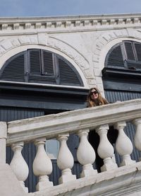 Low angle portrait of woman wearing sunglasses while standing by railing