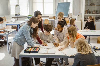 Teacher explaining multiracial students at desk in classroom