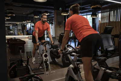 Bearded sportsman riding exercise bicycle and looking at mirror during fitness workout in gym