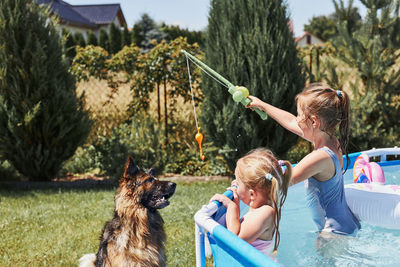 Children playing with dog using a fishing rod toy standing in a pool in a home garden