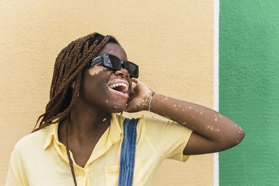 Happy young woman wearing sunglasses standing in front of wall